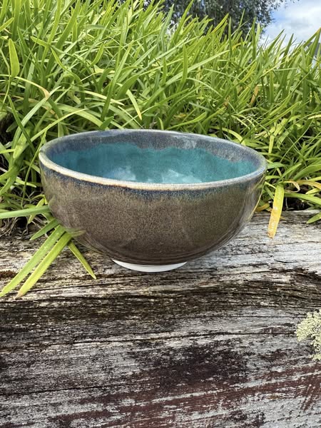 Ceramic bowl with blue interior and brown exterior on a wooden surface with grass in the background