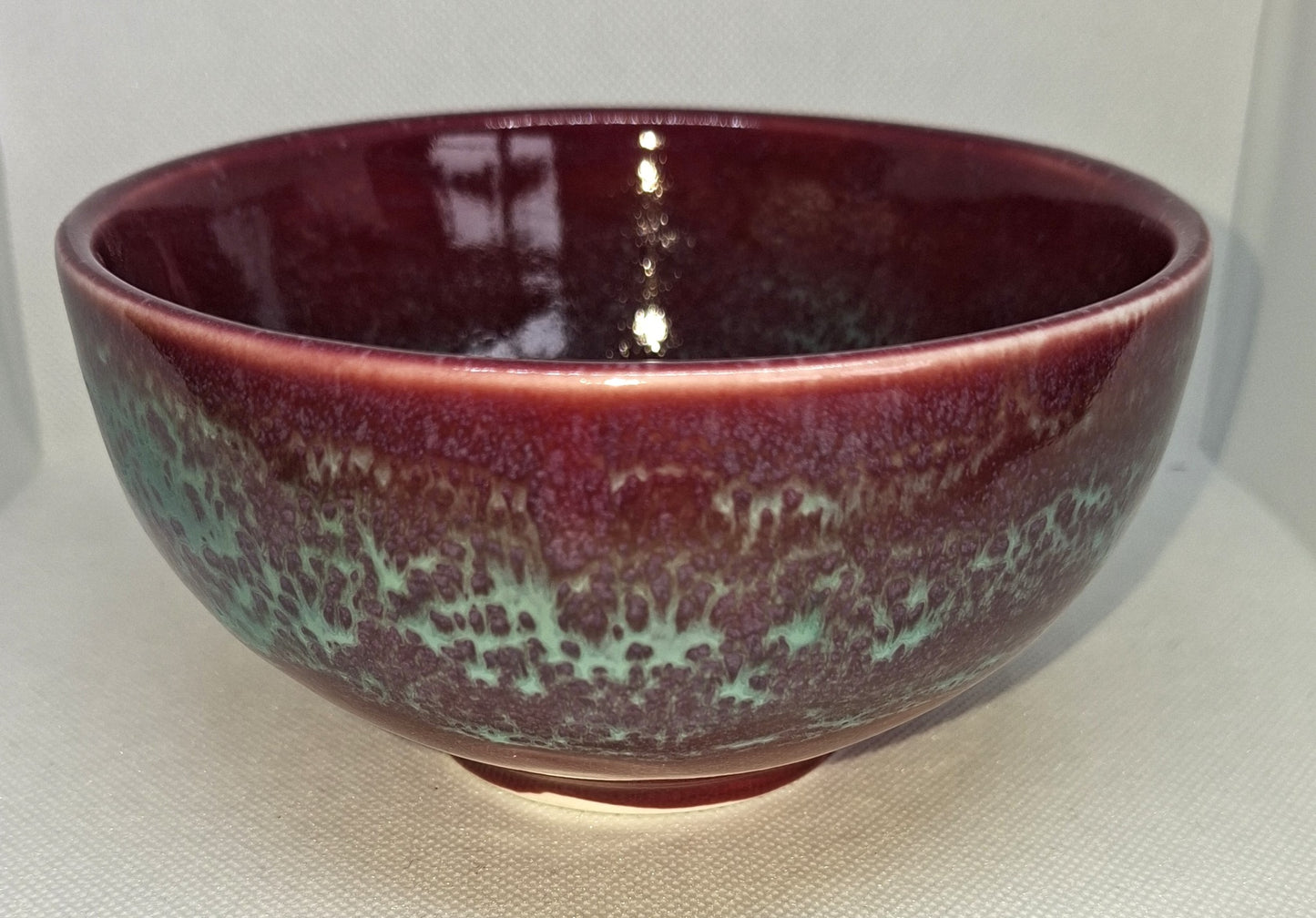 Ceramic bowl with maroon and green glaze on a white background