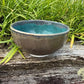 Ceramic bowl with blue interior and brown exterior on a wooden surface with grass in the background