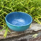 Blue ceramic bowl on a wooden surface with green foliage in the background